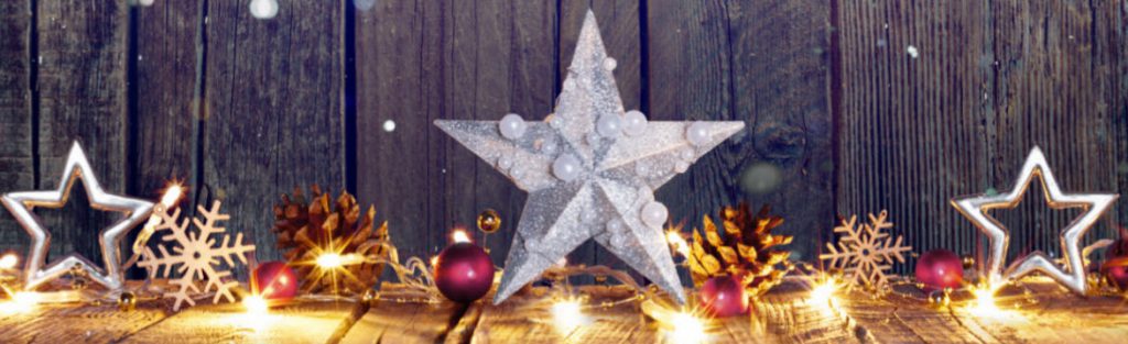 A holiday photo of white lights, stars, pine cones, and snowflakes all on display on a wooden floor with a wood panel background.